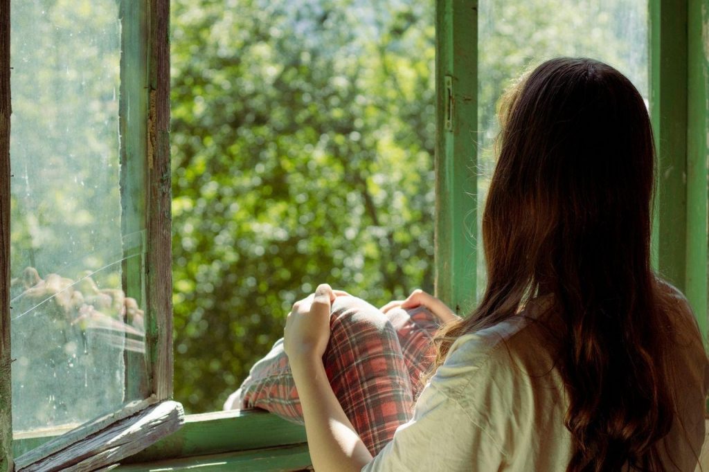 an introvert woman sitting by an open window